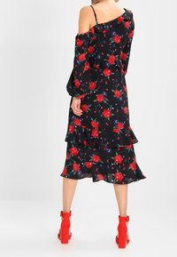 Černé květinové šaty s červenými růžemi a modrými akcenty, off-shoulder design, volánkový lem a dlouhé rukávy. V kombinaci s červenými sandály na podpatku.