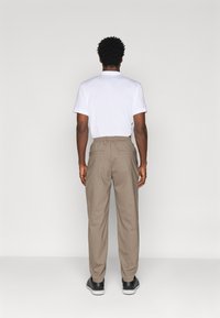 Tricou alb ușor și pantaloni bej cu talie elastică. Pantalonii au două buzunare la spate și o croială lejeră. Sneakerși negri sunt vizibili.