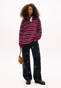 Bordowy sweter w paski z białym kołnierzem, zestawiony z ciemnoniebieskimi szerokimi spodniami jeansowymi ozdobionymi haftowanymi motywami. Mała brązowa torebka na ramię.