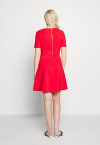 Rotes Kleid mit kurzen Ärmeln und ausgestelltem Rock, mit einem Reißverschluss auf der Rückseite und glattem Stoff. Das Kleid hat ein figurbetontes Oberteil und ein schlichtes Design.