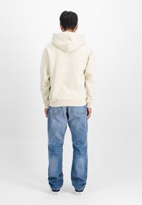 Bežs kapucis ar lielu kapuci, ribota apkakle un apakša, apvienots ar gaiši ziliem džinsiem ar nedaudz bojātu tekstūru.