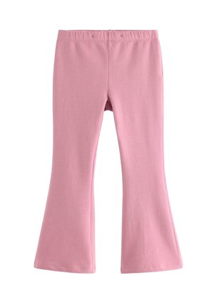 Smilende rødhåret pige står iført pink outfit og brun sweatshirt bundet om skuldrene på hvid baggrund.