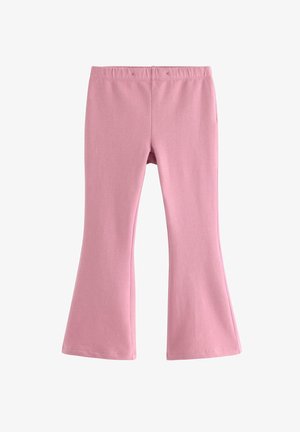 Smilende rødhåret pige står iført pink outfit og brun sweatshirt bundet om skuldrene på hvid baggrund.