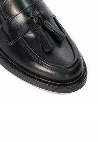 Black leather loafer featuring a high-shine finish, tassel accents, and a rounded toe with decorative stitching along the sole.