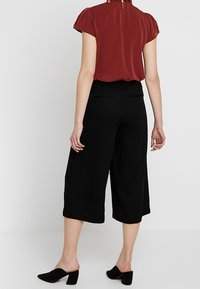 Culottes noirs en tissu doux, dotés d'une taille élastique et de poches latérales. Associés à un haut bordeaux à manches courtes.