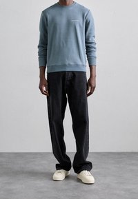Sudadera azul claro con cuello redondo y mangas largas, combinada con pantalones vaqueros negros holgados y zapatillas blancas. Diseño minimalista, sin patrones.