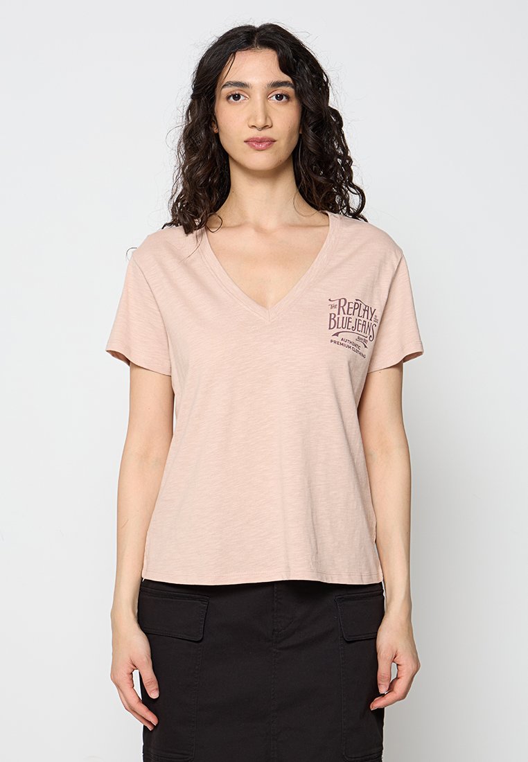 T-shirt a maniche corte con scollo a V in tessuto rosa chiaro con una consistenza morbida; presenta una piccola stampa scura sull'area sinistra del petto.