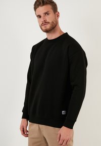 Zwarte crewneck sweatshirt van een katoenmix, met ribgebreide manchetten en onderrand. Een zijlabel voegt een subtiele details toe aan het minimalistische ontwerp.