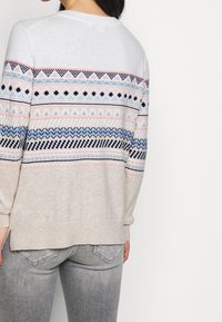 Suéter de punto con patrones geométricos multicolor en azul, rosa y crema. Tiene un cuello redondo y mangas largas, hecho de material suave.