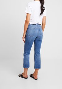 Blå denimjeans med hög midja, raka, korta ben och fransade fållar; kombinerat med en vit t-shirt och svarta, nitarprydda slidesandal.