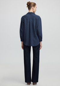 Navyblauwe gestreepte blouse met lange mouwen, knoopmanchetten en detail op de rug. Gepaard met donkere denim rechtvallende broeken.