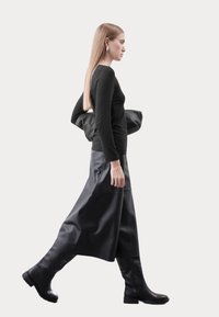 Zwarte lange mouwen top, vloeiende zwarte leren rok en zwarte kniehoge laarzen. Strak ontwerp met gladde texturen en minimale details.