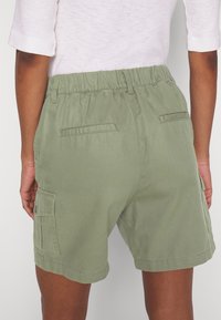 Pantaloni cargo in cotone verde con vestibilità rilassata, cintura elastica e tasche laterali, che mostrano una texture liscia e un design semplice.