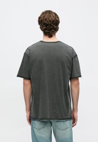 Sötétszürke, túlméretezett póló kerek nyakkivágással, rövid ujjakkal és látható varrási részletekkel. Világoskék farmernadrággal párosítva.