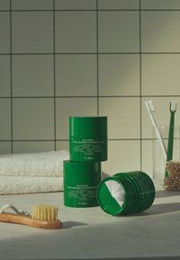 Trzy zielone słoiki oznaczone "Dr.Althea Pure Grinding Cleansing Balm" ułożone na blacie obok drewnianej szczoteczki do zębów, ręczników i akcesoriów łazienkowych.