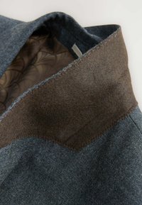 Dunkelblaue Jeansjacke mit einem braunen Filzkragen. Sie zeichnet sich durch eine glatte Textur, kontrastierende Nähte und ein braunes gemustertes Futter innen aus.