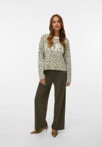 Pull à motif avec imprimé léopard en vert clair et beige, associé à un pantalon ample olive et des chaussures vertes à talons pointus.
