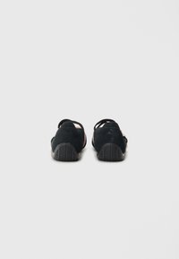 Black suede slip-on shoes with pink accents, featuring a textured rubber sole and cut-out straps for breathability and style.