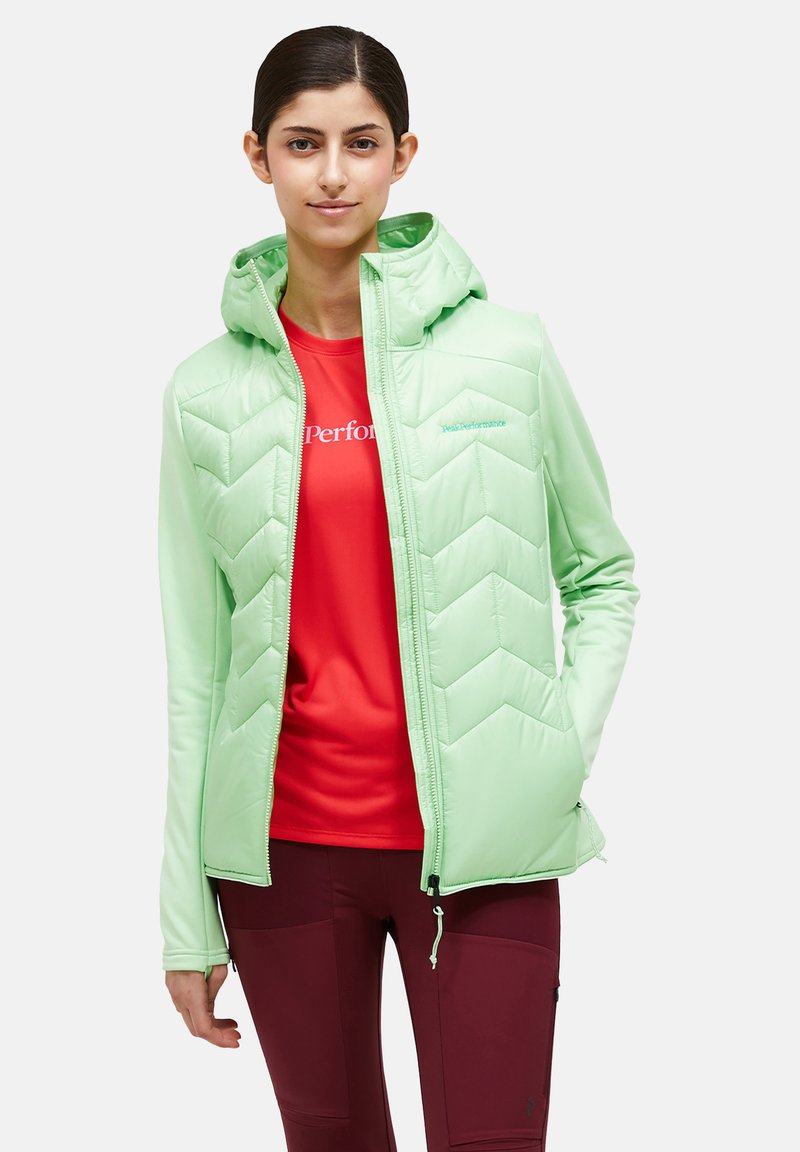 Mint green insulated jacket with a hood features a chevron quilted design, front zipper, and soft texture. Worn over a red shirt.