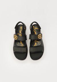 Juodos šlepetės turi tekstūruotą viršutinę medžiagą, reguliuojamas dirželes su auksinėmis detalėmis ir raštuotą įklotą su "Sam Edelman" įrašu.
