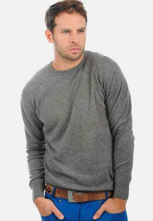 Pull en tricot gris avec un col rond, des poignets côtelés et une texture douce, associé à un pantalon bleu et une ceinture marron.
