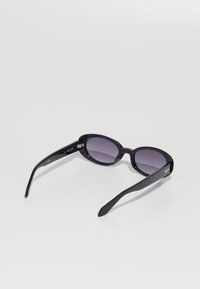 Óculos de sol pretos com armações ovais, lentes escuras, acabamento brilhante e hastes sólidas com um detalhe de logotipo dourado na têmpora.