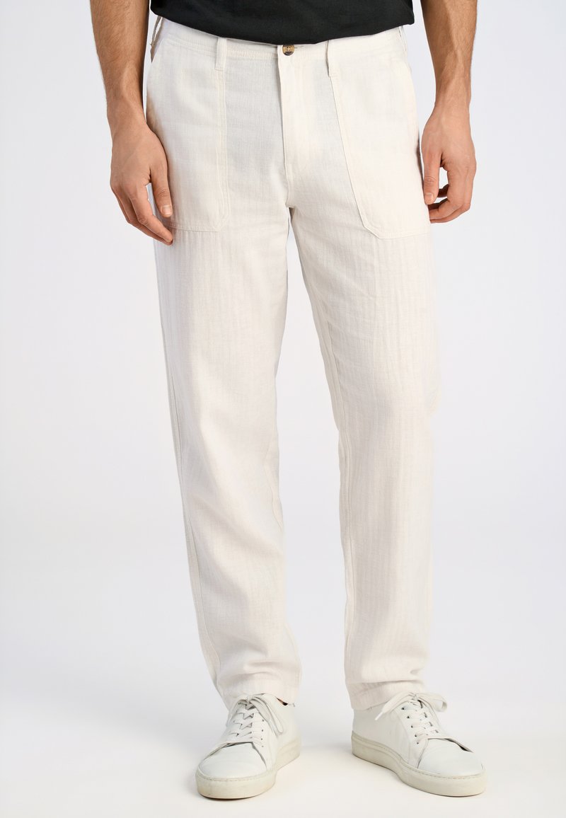 Witte linnen broek met een ontspannen pasvorm, verticale textuur, twee zijzakken en een knoopsluiting. Gecombineerd met witte sneakers.