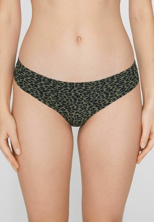 Mujer con braguitas de bikini de cintura baja en verde oliva con estampado de leopardo negro, de pie con las manos relajadas a los lados.