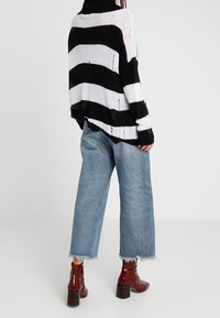 Černobíle pruhovaný oversize svetr s vysokým límcem, kombinovaný se světle modrými širokými kalhotami a červenými kotníkovými botami s robustním podpatkem.