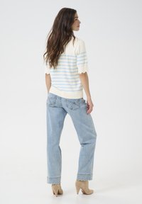 Haut en tricot avec une base crème et des rayures bleu clair, manches courtes à volants. Jean taille haute bleu clair avec ourlet effiloché et poches.