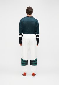 Ανδρικό αθλητικό σύνολο με μακρυμάνικο πουκάμισο από σκουρό πράσινο-μπλε δίχτυ και λευκό παντελόνι με πράσινες και μαύρες ρίγες στο τελείωμα.