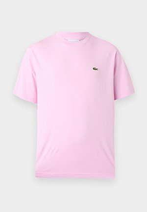 Hellrosa T-Shirt mit kurzen Ärmeln und Rundhalsausschnitt, mit kleinem grünem Krokodil-Logo auf der linken Brust, auf neutralem Hintergrund dargestellt.