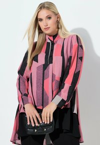 Langærmet skjorte i lyserøde nuancer med dristige sorte geometriske mønstre. Har en høj halsudskæring og knappedetaljer; stylet med en sort håndtaske.