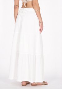 Witte maxi rok met gelaagde ontwerp, textuurstof en elastische tailleband. Gecombineerd met gouden sandaaltjes voor een neutrale esthetiek.