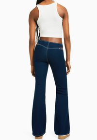 Rozšířené modré džíny z denimu s kontrastním bílým prošíváním a kostkovaným detailem na pásu, kombinované s upnutým bílým tílkem.