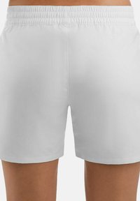 Vista trasera de una persona que lleva puestos unos pantalones cortos de cintura elástica blanca, mostrando el ajuste y la longitud por encima de las rodillas.