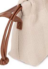 Bolso de lona en beige con superficie texturizada; cuenta con adornos de cuero marrón y asas anudadas para su cierre. Forma compacta y redondeada.
