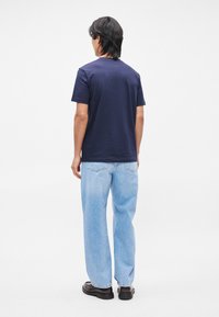 Μπλε βαμβακερό t-shirt με κοντά μανίκια, συνδυασμένο με ανοιχτού μπλε τζιν ίσιας γραμμής και σκούρα παπούτσια, απεικονιζόμενο από πίσω.