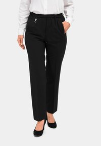 Schwarze Hose mit lockerer Passform, elastischem Bund, seitlichen Taschen und einem silbernen Akzent am Bund, kombiniert mit schwarzen Absätzen.