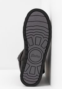 Schwarze Sneaker mit strukturierter Gummisohle im Wellenmuster, die das 'Skechers'-Logo in der Mitte zeigt. Seitenansicht vor einem wei�ßen Hintergrund.