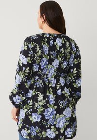 Floral blouse in zwart met blauwe en groene bloemen. Gathered textuur aan de achterkant, lange puff mouwen en een losse pasvorm.