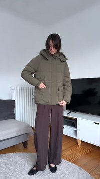 Olive green puffer jacket with a hood, front zipper, and two side pockets. Features quilted design and elastic cuffs, worn over brown pants.