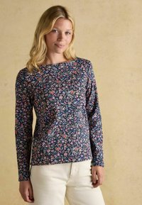 Dlhý rukáv kvetinového topu s námorníckou základnou a ružovými a modrými kvetmi, okrúhly výstrih a priliehavý strih. V kombinácii so svetlými nohavicami.