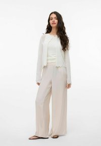 Kergest valgest kudumist cardigan'ist, mis on kantud heleda kreemja topi ja laia jala helebeezide pükstega, millel on narmastega äärega ja lõdva lõikega.