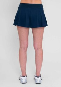 Falda deportiva de color azul marino con un diseño acampanado, cinturilla elástica y textura de tela suave. Combinada con zapatillas blancas y grises.