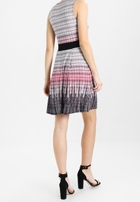 Bezramínkov dress s černým pasem, který má gradientní vzor od světle šedé po tmavě fialovou, doplněný o černé vysoké podpatky.