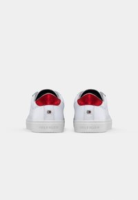 Zapatillas blancas con un acabado suave, con detalles de gamuza roja en el talón y una suela de goma texturizada. Marca visible en el talón.