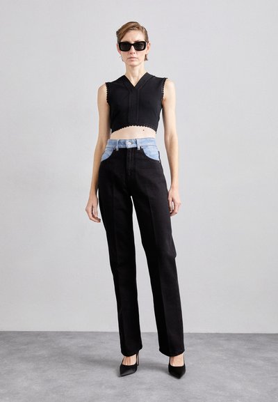 Top court noir avec des bords festonnés, associé à un jean noir taille haute avec un panneau en denim clair à l'avant, porté avec des talons noirs.