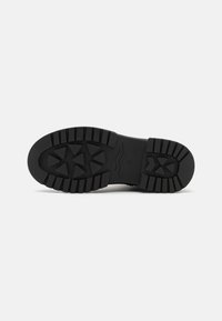 Semelle de chaussure en caoutchouc noir avec un motif de texture en relief comprenant des rainures triangulaires et horizontales pour une meilleure adhérence. Profil plat, sans branding visible.