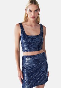 Top corto in paillettes blu navy e minigonna abbinata con scollatura quadrata e design aderente, che mette in mostra texture riflettenti e una finitura liscia.